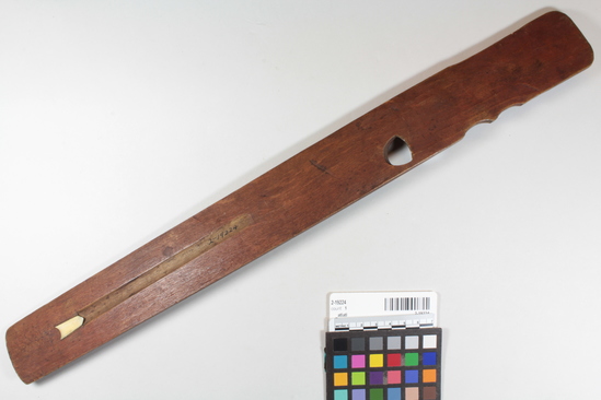 Hearst Museum object titled Atlatl, accession number 2-19224, described as Flat, wooden. Painted red on flat "business" surface which has bone spur at end of groove; traces of black and red pigment on obverse; palm grip; engraved ownership mark near index finger hole.