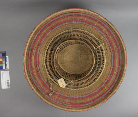 Hearst Museum object titled Hat, accession number 10-1282, described as Woven fiber hat; spiral designs; natural; brown plaid; round; peaked; red tassel; splint lining wrapped with red, purple thread; plaited rattan head ring; 15” dia.