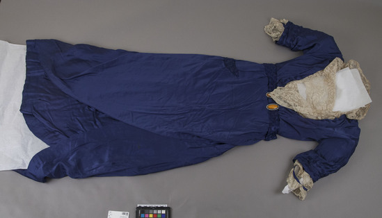 Hearst Museum object titled Dress, accession number 7-7269, described as Dress made of silk and rhinestones with a yellow stone buckle. Ssatin long tunic over satin, lace inset in bodice rises to make wired collar in back. Blue, Made by Allen et Cie,  106 New Bond St.