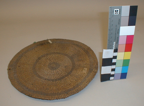 Hearst Museum object titled Sifting tray, accession number 1-11666, described as Sifting tray for acorn meal; twined. Warp is Hazel (Corylus cornuta californica), weft is Sugar pine (Pinus lambertiana). White pattern is Beargrass (Xerophyllum tenax). Hazel strengthening fibers. Dirty from use. Plain twined, almost completely overlaid. White, mostly single faced overlay, some 2 faced. 2 rows of lattice twined rods (on back) near rim and center.