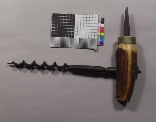 Hearst Museum object titled Corkscrew, accession number 7-9170, described as Corkscrew, tee handle; antler handle (broken) with spike at one end, secured by nickel plated brass ferrule; machined iron shank inserted into handle, secured by ring holder; cyphered center worm point. Materials/techniques: iron, antler, machining, brass, nickel plating. Context of use: wine bottle cork puller with spike for breaking sealing wax.