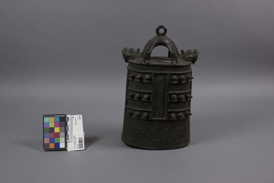 Hearst Museum object titled Bronze bell, accession number 9-6730, described as Bronze bell with spike-like protrusions (mammae); Greek key design at base with incised stylized lion heads directly above; 2-headed dragon handle; no clapper; height 10.5 inches. Copy of ancient bell.