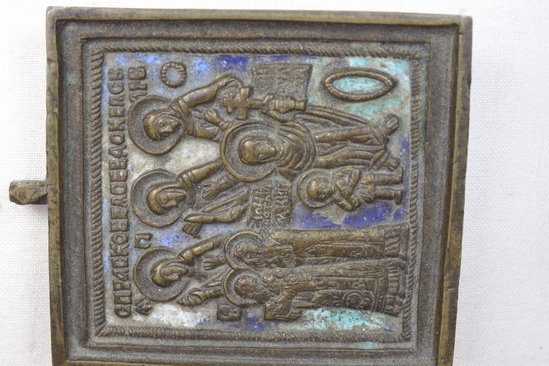 Hearst Museum object titled Cast brass icon, accession number 7-9062, described as Icon, cast brass with enamel ground; three saints at top, all facing towards left; their names abbreviated and run together. Above; two bishop/saints. Lower left: child with saint holding the “Eight Pointed Cross;” name of one bishop or the child is John, with saint with cross is “Smoulita;” green, blue and white enamel ground. right third of a tryptich; height 5.5 cm, width 5.1 cm. Holy image associated with worship. According to George Shkurkin, who identified figures, these are local saints. The small child is probably a martyr; the saint who holds a cross is probably one who has converted an ethnic group. “Smoulita” is a local saint, not known to Mr. Shkurkin.