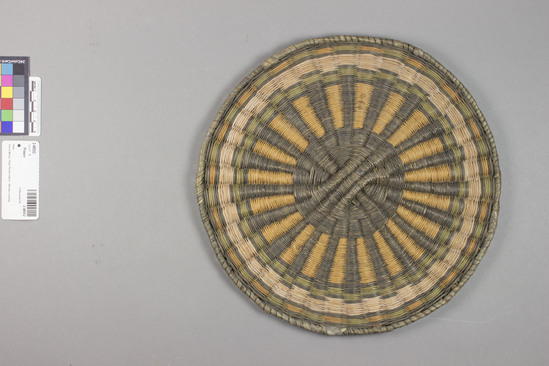 Hearst Museum object 2 of 3 titled Plaque, accession number 2-48552, described as Wickerweave; radiating black and yellow lines from black center; alternating green and yellow areas inside perimeter. Made of ribs of sumac or willow twigs, rabbit brush weft, yucca leaf wrapped edge.