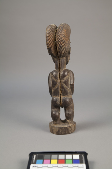 Hearst Museum object 3 of 4 titled Figure, accession number 5-7682, described as Figure; wood; female, standing, with hands on stomach; elaborate incised hair-do; hatch markings  on face, neck and back; white filled eyes; protruding navel; Heavy general wear, split down back. Evaluation: $ 700.00