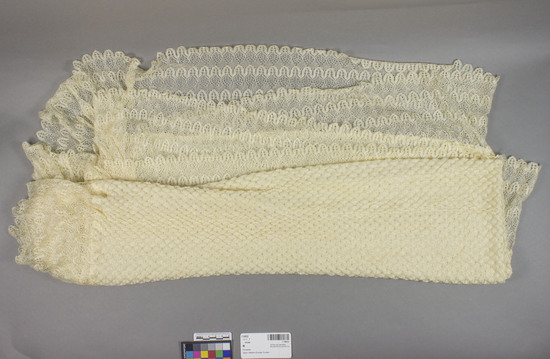 Hearst Museum object titled Shawl, accession number 7-10032, described as Spanish machine-knitted rectangular shawl, blonde color, with lace border, gathered at corners.  Body of shawl is approx. 126 x 74 cm. (stretched moderately flat), plus 13.5 cm. lace border; overall size 152.5 x 98 cm.  Lace border technique not known.