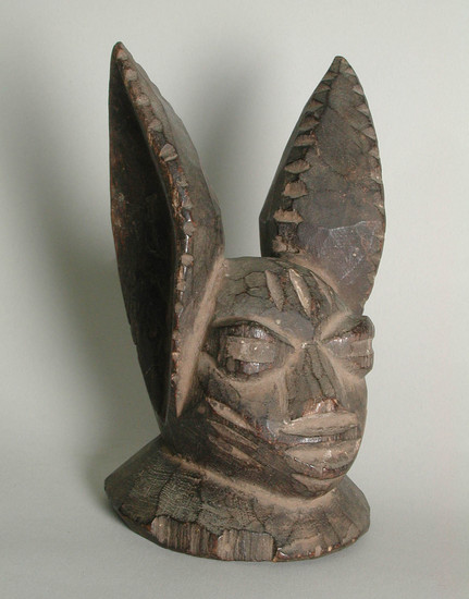 Hearst Museum object titled Mask, accession number 5-16221, described as Yoruba model Egungun (hare) mask. Abeokuta . carved wood mask model.  human-like features, eyes, nose & mouth with rabbit ears. Purchased from Old Curiosity Shop, L.A. Conservation: Drying crack along base of left ear and down side of left neck base.