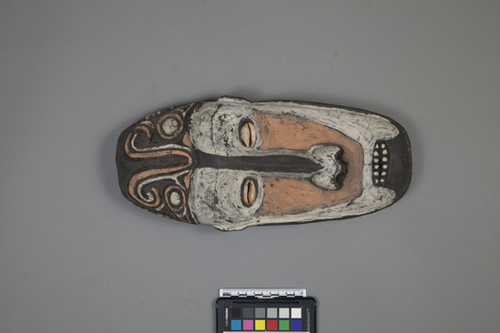 Hearst Museum object titled Board mask, accession number 11-37777, described as Mask, small board type, of carved wood; inlaid cowrie shell eyes; mouth slightly open to show teeth; incised curvilinear designs above brow; painted black, white, and pink