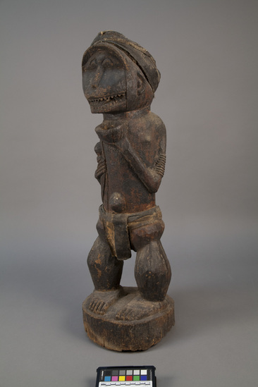 Hearst Museum object titled Figure, accession number 5-3228, described as Carved wooden figure. Standing male with monkey-face and protruding umbilicum. Left hand holding cup under chin. Right hand grasping dagger; cotton loin cloth and head band. Also has protuding umbilicum.