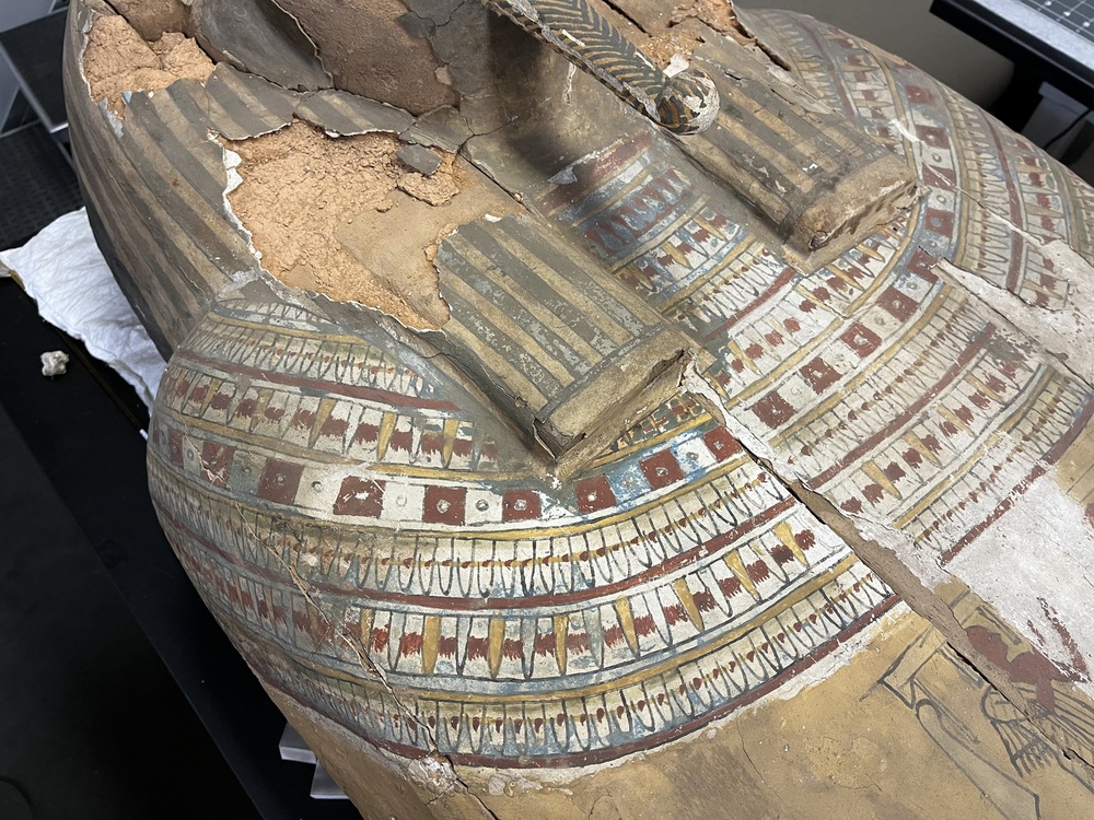 Hearst Museum object 22 of 167 titled Coffin, accession number 6-19912, described as Wooden anthropoid coffin. Inscription running down center of lid. Determined by Kea Johnston to probably be the outer coffin of Iwefaa (6-19928, 12-11039). According to Kea Johnston, "This coffin belonged to a man named Iwefaa, whose name is inserted in the middle of the spells written in the two columns on the front. This coffin is likely the outer coffin for PAHMA 6-19928 based on the similarity of the owner's name, unusual costume, and the paleography of the inscription. Both coffins were purchased on the antiquities market by George Reisner for Phoebe A Hearst. However, stylistically, they are very similar to a set of coffins known to have come from the site of Akhmim, which was excavated in the 1880s by Gaston Maspero, and which has heavily looted for the antiquities market during this decade." "The pectoral vignette between the text and the collar shows the deceased standing before squatting baboon and is the source of our logo. The hieroglyph for 'sky' is above their heads, and the side borders are formed by a pyramid and the symbol for the West.