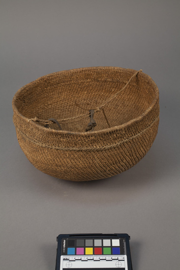 Hearst Museum object titled Basket woven, accession number 5-13764, described as Murub., Kenya; Gob Wambili; Rendille. August, 1979. 5-13764, acc no. 3433. Orig. No 4. File code: 1.3 Collector: Jean Colvin. Donor: Jean Colvin. Materials, techniques: Ergeg woven for bottom and rim, meda used for main body; both used to make basket more beautiful. Coiled split stick basketry. Context of use: Used as bowl or plate mornings and evenings, for milking camels and eating meat. Used by anyone. Always made by women. This one made by Ronguma woman in 1979, new and never used. Flatter than most. Took several months. This is the second one she made. Round ones like this are easier to balance while milking than the conically-shaped murub. Description: Bowl, basketry; coiled split-stitch basketry bowl; 2-ply cordage handle with pendant leather strap across top; d. 31 cm. h. 18.3 cm. References: for further information see field sheet #JC4.