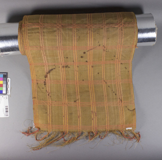 Hearst Museum object titled Mat, accession number 11-42806, described as Fiber strip, woven; orange, yellow plaid pattern on tan background; geometric edge pattern; worn and stained. 210.0 cm. x 36.0 cm.