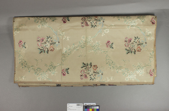 Hearst Museum object titled Textile sample, accession number 7-6798, described as Rayon?  Plain weave, brocaded. Grey and red warp striped ground, varicolored designs.  Floral motives.  27 inches by 50½ inches.