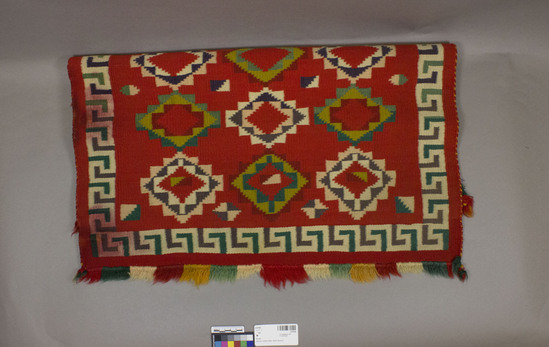 Hearst Museum object 2 of 3 titled Rug, accession number 2-47020, described as Germantown with multicolor fringe on warp ends; red ground, 3 rows multicolored terraced diamond designs; inner border alternating green and purple right angles on white ground; water damage along one side.  Germantown wool yarn; tapestry weave.