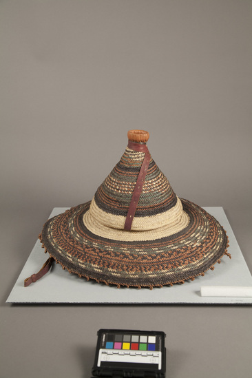 Hearst Museum object titled Basketry hat, accession number 5-3096, described as Basketry hat; Malfa; fiber, wide brim; cone shaped top; multi-colored decoration, black, red, green; red leather chin strap.