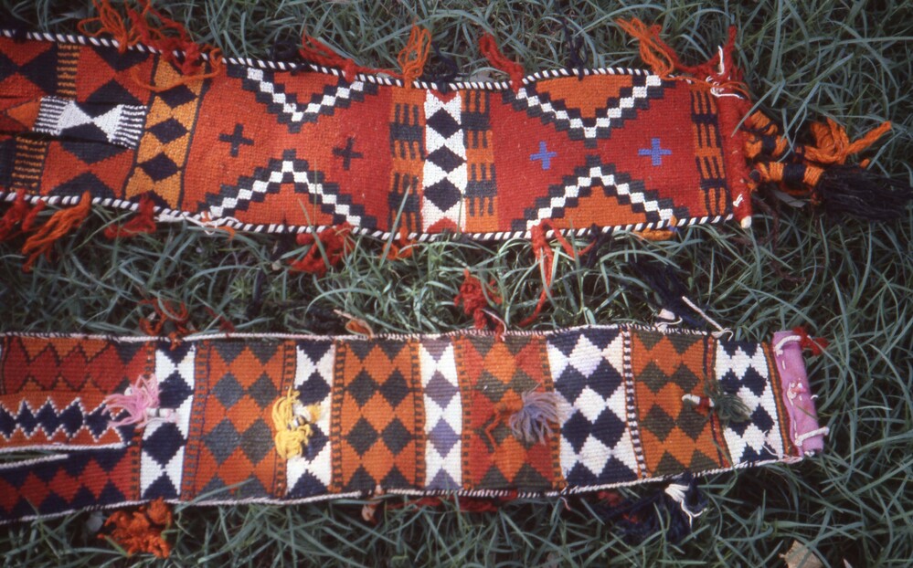 Hearst Museum object titled Color slide, accession number 25-25192, described as 35mm color slide transparency. Close-up of textile with diamond patterns; featuring tassel detailing; colored red, orange, blue, purple, black, and white.