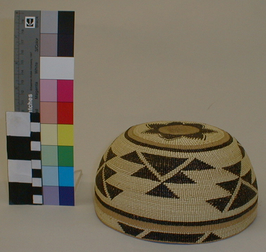 Hearst Museum object titled Hat, accession number 1-258617, described as Basketry. Round, circular design of stepped triangles in dark brown with stripes of dark and light brown at top and bottom. Seven point star on top in dark and light brown, on straw colored ground.  Conifer root, white grass, maidenhair fern, plain twined with half twist overlay.