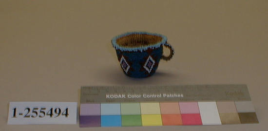 Hearst Museum object titled Basket, accession number 1-255494, described as Basketry teacup. Cup is covered with glass seed beadwork, multi-colored geometric design on bright blue ground. Plain twined, tule.