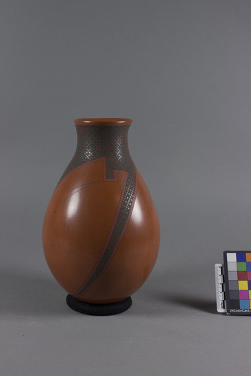 Hearst Museum object titled Vessel, accession number 3-32018, described as Pottery vase made by Jerardo Tena, a Mata Ortiz artist, on September 10, 2005.  Red polished ceramic with matte black checkered design outlined in red.  Majority of the decoration is on the neck of the vessel with three evenly spaced points swooping down lower.