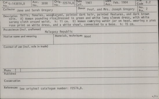Documentation associated with Hearst Museum object titled Dolls, accession number 5-14381a,b, described as Dolls: females, wood carved, painted dark hair, painted features, and dark brown skin. (A) Woman pounding rice is dressed in green and white long sleeve dress, with white sarong cloth around waist. Height 11 cm. (B) Woman carrying water jar on head, wearing a pink rose print on white dress, and a white shawl, connected to a base. Height 15 cm.