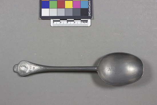 Hearst Museum object titled Spoon, accession number 7-2007, described as Spoon; pewter, cast; plover egg shaped bowl with rat tail handle; lobed handle end with women’s heads with circular frame relief; curvilinear design on rat-tail bowl back connection handle, back hallmarked with W; 7-1998-2007 are a set; length 18.5 cm.