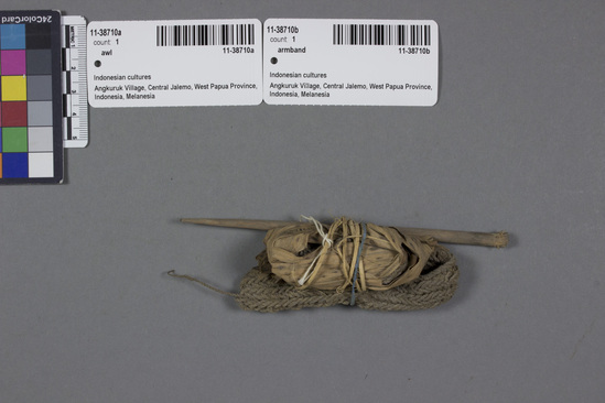 Hearst Museum object titled Wood awl w/ incomplete armband wrapped in grass, accession number 11-38710a,b, described as Arm band in process; a) Looped bast band for attachment of cowrie shells; b) wood awl; In 1962 two cowries = one day’s work; in 1966 six cowries = taro tube.  No one could work in immediate vicinity of mission