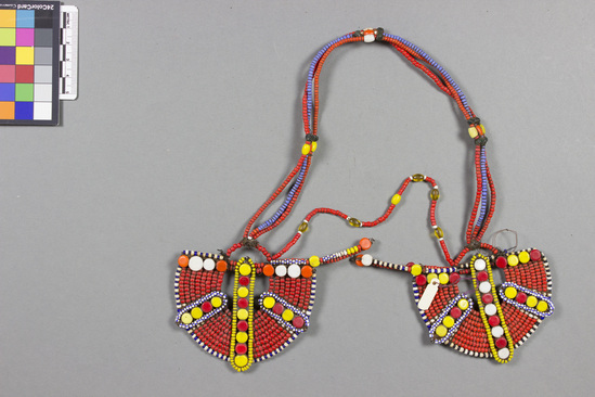 Hearst Museum object titled Beaded ornaments, accession number 5-13765, described as Beaded ornaments., Kenya; Gob Wambili); Rendille. August, 1979. 5-13765, acc no. 3433. Orig. No. 6. File code: 2.2 Collector: Jean Colvin. Donor: Jean Colvin. Materials, techniques: Glass and plastic beads and ornaments, buttons wire, fiber; rubbed with ocher and animal fat. Context of use: Worn by putting string over top of had with earrings hanging over ears. Worn by young girls before they are of marriageable age. Cf. 5-13352. Description: Earrings; hemispherical beaded earrings connected by 3 strands beadwork; red, blue, white seed beads; rd, yellow, orange, white flat round ornaments; beads and ornaments over leather and wire; w. ea. hemisphere 8.5 cm. References: Field sheet JC6.