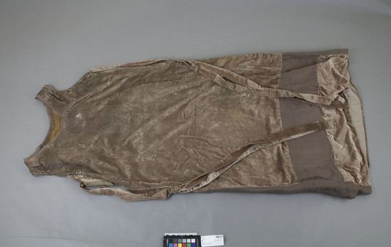 Hearst Museum object titled Evening gown, accession number 7-7225, described as Gown; evening gown, lame(?); Fortuny fabric; taupe silk velvet with gold painted silk screen print of curvilinear designs and confronting dragon-like animals; sleeveless; round neck; self ribbons at sides; front length 1.16 M