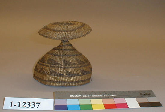 Hearst Museum object titled Cap, accession number 1-12337, described as Child's cap; twined. Warp is twisted Tule (Schoenoplectus acutus), weft is also twisted Tule. White pattern is Reed (Phragmites vulgaris). Brown color is mud-dyed Tule. The crown of this cap had feathers placed in it during ancient times. Height: 14.0 cm, Diameter: 16.0 cm.