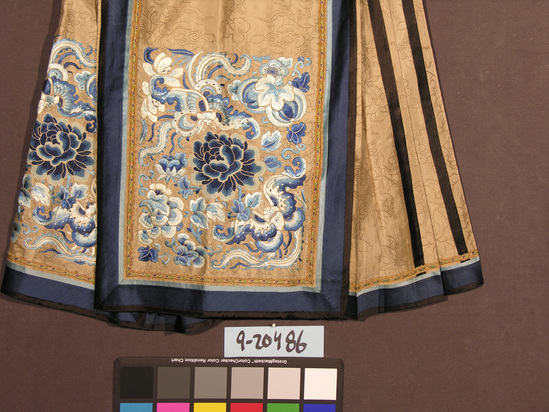 Hearst Museum object titled Skirt, accession number 9-20486, described as Beige silk brocade wedding skirt. Side pleats appliqued with black stripes. Beautiful blue/white silk(?) embroidery at bottom of panels, front and back. Panel framed with blue/light blue stripes and multi-color, patterned ribbon trim. Black waistband.