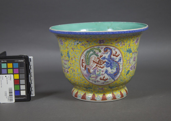 Hearst Museum object 3 of 7 titled Vase and dish, accession number 9-16249a,b, described as Vase w/dish; enamel on porcelain; exteriors yellow ground w/ pink, green and blue floral motifs, blue fret band around edge, reign marks on undersides;  (a). vase:  squat w/wide mouth, pedestal base; 3 medallions w/dragon motif; 3 perforations in bottom;  h.  19.2 cm.;  (b)  dish; green-blue interior glaze, one area abraded;  d.  22.5 cm.  Porcelain w/enamel colors; glaze.  Vase.  China attr.