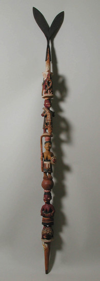 Hearst Museum object 1 of 7 titled Staff, accession number 5-14943, described as staff, carved and painted wood;  from pointed base are woman w/ baby on back, standing woman holding staff, man wrestling with crocodile and rooster w/ snake in mouth; ocher colors + black;  bifurcated iron ornament representing fishtail attached at top;  l. 128.4 cm.