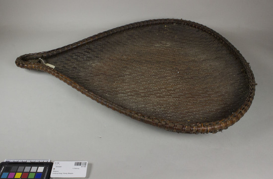 Hearst Museum object titled Winnower, accession number 18-1108, described as Basket: winnowing basket. Tear drop shaped, brown. Body material not known, rattan frame. Damaged. Used to winnow rice or other materials. To separate different grades of pounded flour. Made by aboriginal tribe, Sakai? Bought in local markets and used by women. Some “niru” are also made locally by women only, but the better quality specimens are purchased and said to be made by an “orang asli” tribe. Cost in U.S. dollars: 1.25. Length 71.5 cm. Width at widest 50 cm.