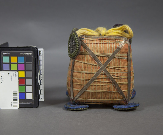 Hearst Museum object titled Work basket, accession number 9-14563, described as Workbasket, funeral decoration; cube covered with orange cloth wrapped with yellow cordage. Discs in each corner (one missing) faced with metal beads; yellow wool yarn and two discs at top as hanging device; height: 15 cm.