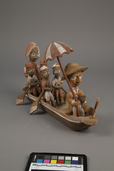 Hearst Museum object 7 of 15 titled Figures, accession number 5-16237a-q, described as caricature figure group; caricature of a District Officer on tour; carved & painted wood a - boat, has bag of frags b - Dist. officer (front) c - poler (rear) d - paddler (LF) e - paddler (LR) f - paddler (RF) g - paddler (RR) h - hat i - umbrella handle j - umbrella k - flag l - pipe m - pole n - paddle (RF) o - paddle (LF) p - paddle (LR) q - paddle (RR) Found two pegs in a bag with this object number.