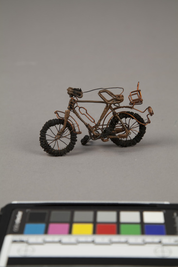 Hearst Museum object titled Bicycle figure, accession number 5-17019, described as Miniature bicycle made of copper wire and black rubber bands (which are wrapped around the wire base of the wheels, pedals and handle grips.  1987.