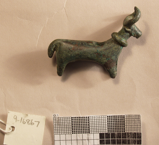 Hearst Museum object titled Bovine pendant, accession number 9-16867, described as Pendant in the form of a long-horned bovine.  Wears collar; tail hangs down; square muzzle; recurved horns.  Pierced through back vertically for suspension.  Hollow body, ears articulated.  Green patina.  L. 5.6 cm.  Ht. 4.6 cm