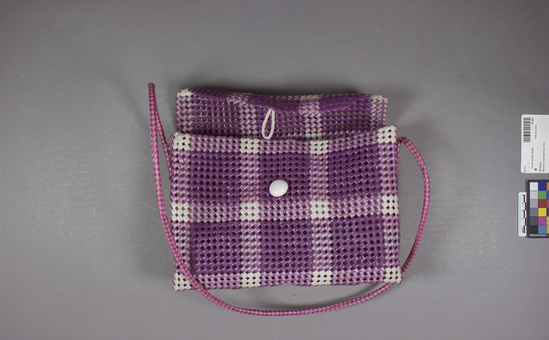 Hearst Museum object titled Woven plastic purse, accession number 18-462, described as Purse: plastic, plaited and folded purple and white plastic; plaited handle. “ganefo”= (purse of the games of the new emerging forces) (competitor of Olympics). Height without handle 19 cm. Width 27 cm.