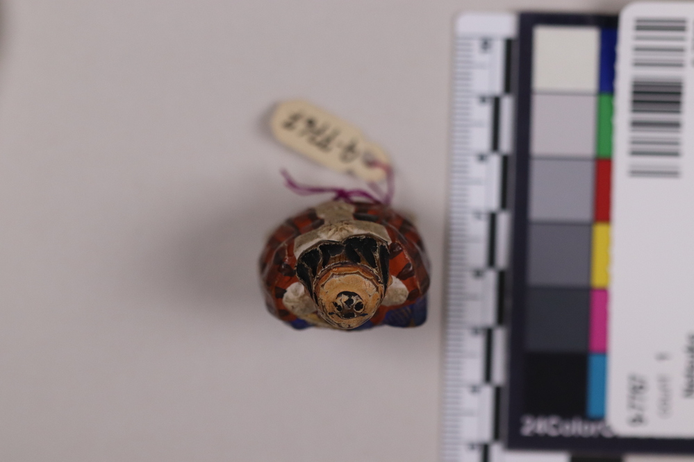 Hearst Museum object titled Netsuke, accession number 9-7767, described as Netsuke: man carrying fan in right hand. Wears red coat with black stripes, blue trimming. Hat.