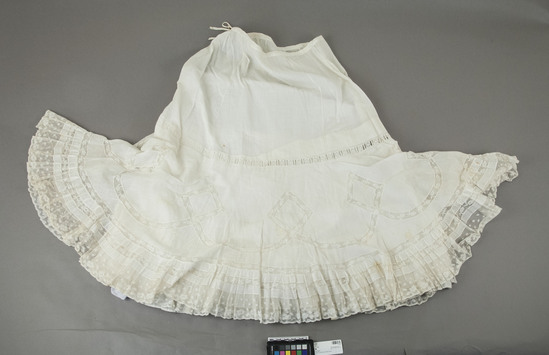 Hearst Museum object titled Dress, accession number 7-7187, described as Petticoat. Materials: Batiste, lace. Techniques: sewing. Colors: white. Dimensions: 37 inches long center front. Remarks: Long, white batiste, petticoat with drawstring waist. Single layer, gored, top half joined to double ruffle. Under ruffle is lace trimmed at bottom, out-ruffle is circularly cut with much val lace insertion. Strip of beading insertion where ruffles join top half of insertion. Strip of beading insertion where ruffles join top half of skirt. Monogram NJD at waistline. Tuck made inside to shorten. Slight stains. Goes with 3625.