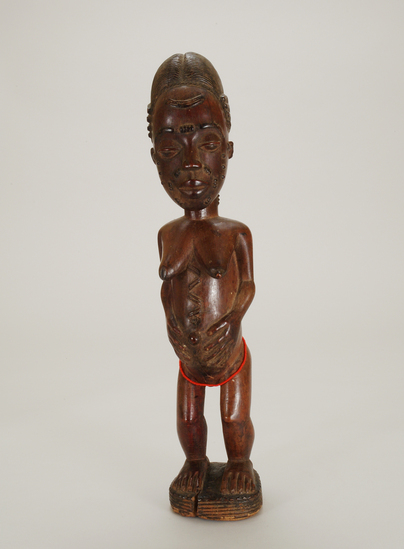 Hearst Museum object titled Figurine, female, accession number 5-3182, described as carved wooden figure; standing female with hands clasped around protruding umbilicum; string of red beads around thighs;