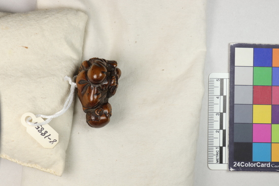 Hearst Museum object titled Netsuke, accession number 9-18851, described as Netsuke; seated man (farmer), sharpening sickle and smoking a pipe; bald head; right leg bent under him; H 3.7 cm X W 3.4 cm