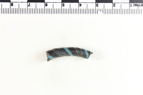 Hearst Museum object 3 of 6 titled Bracelet fragment, accession number 9-8049, described as Glass bracelet frag.; opaque black, twisted, curved rod w/ blue spiral; 27 x 7 mm.