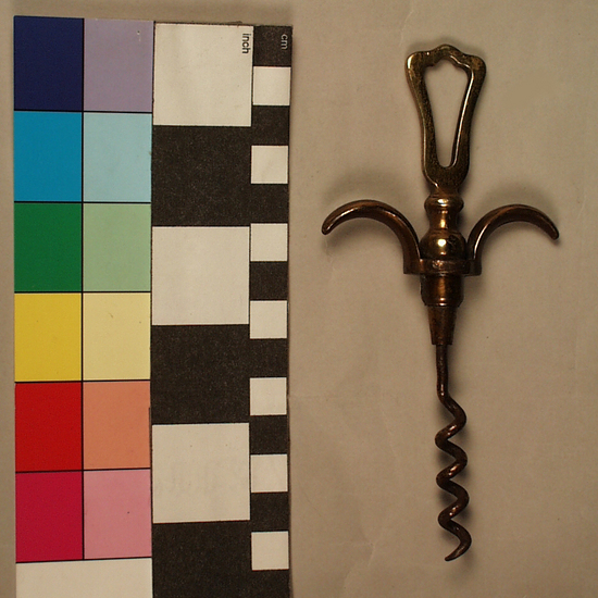 Hearst Museum object titled Corkscrew, accession number 7-9228, described as Corkscrew, eyebrow handle; cast brass two-finger pull handle, abstract triangular hollowed out form atop handle; brass plated iron wire helical worm. Wine bottle cork puller.