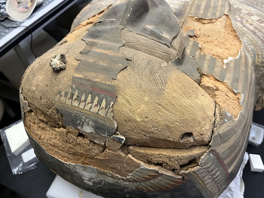 Hearst Museum object 151 of 167 titled Coffin, accession number 6-19912, described as Wooden anthropoid coffin. Inscription running down center of lid. Determined by Kea Johnston to probably be the outer coffin of Iwefaa (6-19928, 12-11039). According to Kea Johnston, "This coffin belonged to a man named Iwefaa, whose name is inserted in the middle of the spells written in the two columns on the front. This coffin is likely the outer coffin for PAHMA 6-19928 based on the similarity of the owner's name, unusual costume, and the paleography of the inscription. Both coffins were purchased on the antiquities market by George Reisner for Phoebe A Hearst. However, stylistically, they are very similar to a set of coffins known to have come from the site of Akhmim, which was excavated in the 1880s by Gaston Maspero, and which has heavily looted for the antiquities market during this decade." "The pectoral vignette between the text and the collar shows the deceased standing before squatting baboon and is the source of our logo. The hieroglyph for 'sky' is above their heads, and the side borders are formed by a pyramid and the symbol for the West.