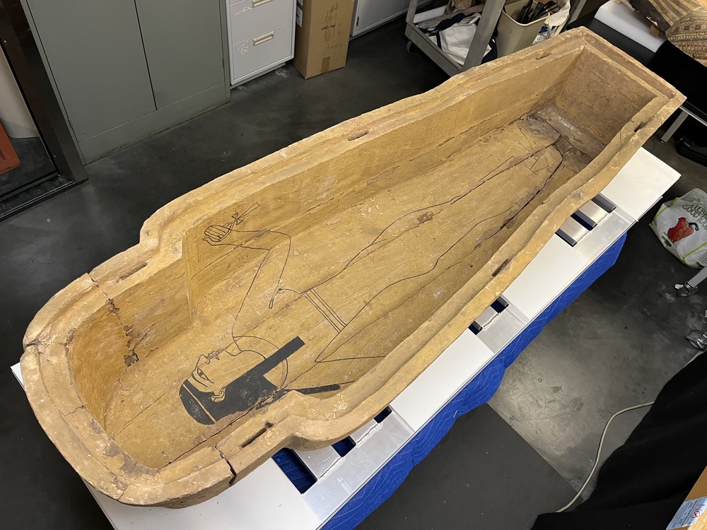 Hearst Museum object 105 of 167 titled Coffin, accession number 6-19912, described as Wooden anthropoid coffin. Inscription running down center of lid. Determined by Kea Johnston to probably be the outer coffin of Iwefaa (6-19928, 12-11039). According to Kea Johnston, "This coffin belonged to a man named Iwefaa, whose name is inserted in the middle of the spells written in the two columns on the front. This coffin is likely the outer coffin for PAHMA 6-19928 based on the similarity of the owner's name, unusual costume, and the paleography of the inscription. Both coffins were purchased on the antiquities market by George Reisner for Phoebe A Hearst. However, stylistically, they are very similar to a set of coffins known to have come from the site of Akhmim, which was excavated in the 1880s by Gaston Maspero, and which has heavily looted for the antiquities market during this decade." "The pectoral vignette between the text and the collar shows the deceased standing before squatting baboon and is the source of our logo. The hieroglyph for 'sky' is above their heads, and the side borders are formed by a pyramid and the symbol for the West.