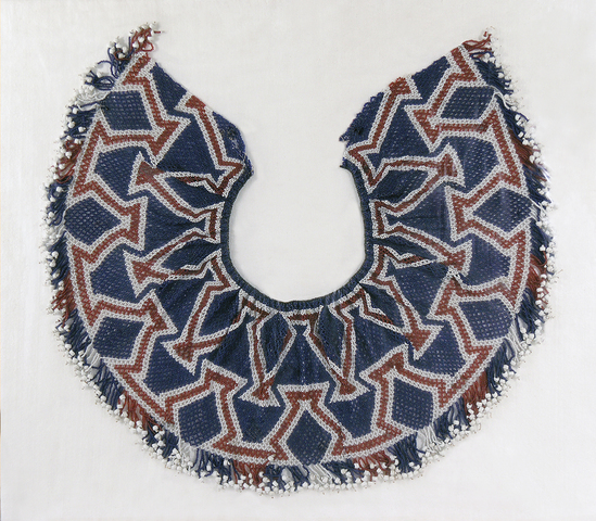 Hearst Museum object 1 of 2 titled Collar or cape, accession number 1-13867, described as Bead collar or cape; red, white, and blue.  Intricate geometric pattern of glass beads.  Bottom decorated with many single strands of tiny solid glass beads with large glass bead at end.