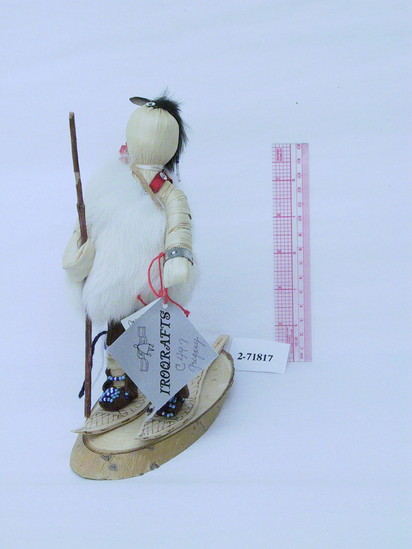 Hearst Museum object titled Doll, accession number 2-71817, described as Cayuga [Turtle Clan] doll.  H = 8”, on base.  Corn husk, with no features.  Black rabbit fur scalp lock, w/ bead dangles & feather ; wooden snowshoes.  Brown leather, high backed mocassins, beaded, blue-white yarn.  Knee wraps w/ “tails”.  Brown suede breeclout, red tie.  White rabbit fur, one-armed jerkin w/ red strap for the red felt blanket tied to back.  Has silver arm band and carries a pole in right hand.