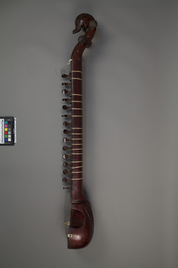 Hearst Museum object titled Esraj, accession number 9-11932a, described as Esraj (violin-like stringed instrument) with bow; round wood soundbox, membrane-covered, with long neck culminating in curved pegboard with carved dolphin head at rear; on one side is wood panel with 15 sympathetic strings;4 main strings; all strings are steel or brass; ivory bridge. Length: 96 cm; width: 15 cm.