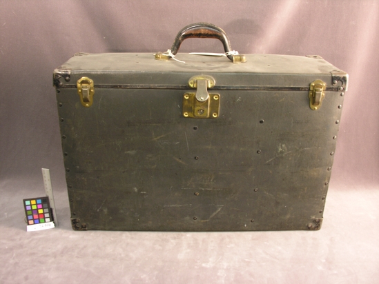 Hearst Museum object 2 of 3 titled Camera and case, accession number 2-72016a,b, described as (a) Camera Transport Case:  Paperboard w/ green fabric lining; interior divided into three sections.  Metal clasps and fixtures , top mounted carrying handle.  One end mended w/ interior board nailed to paperboard.  Drop down shelf rests on section dividers.  H=38.5cm; W=59.5cm; T=18.6cm.  (b) Key for case [tied to handle]